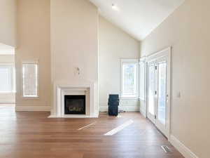 Unfurnished living room with high vaulted ceiling, a glass covered fireplace, and wood finished floors