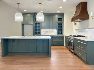 Kitchen with glass insert cabinets, backsplash, custom range hood, and recessed lighting