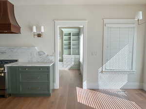 Kitchen featuring premium range hood, green cabinets, stainless steel range with gas stovetop, dark wood-type flooring, and light stone counters