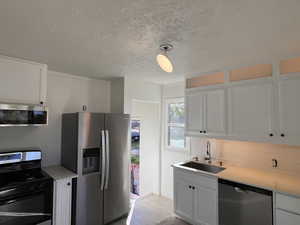 Kitchen with appliances with stainless steel finishes, white cabinetry, a textured ceiling, tasteful backsplash, and hanging light fixtures