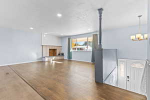 Unfurnished living room with wood finished floors, a chandelier, recessed lighting, a fireplace, and a textured ceiling