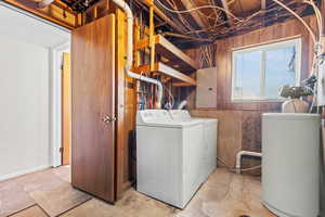 Laundry room with electric panel, wooden walls, washer and dryer, and concrete floors