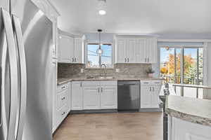Kitchen with appliances with stainless steel finishes, pendant lighting, white cabinets, tasteful backsplash, and recessed lighting