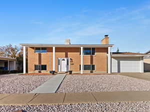 Split foyer home featuring driveway, a chimney, brick siding, and a garage