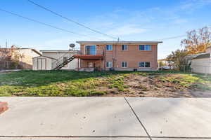 Rear view of house with stairway, a storage shed, brick siding, a deck, and a patio area