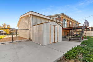 View of property exterior featuring a storage shed, a patio area, stairway, a gate, and brick siding