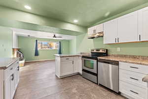 Kitchen featuring white cabinetry, appliances with stainless steel finishes, a peninsula, under cabinet range hood, and recessed lighting