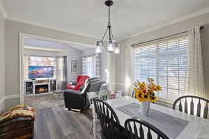 Dining space featuring wood finished floors, a warm lit fireplace, ornamental molding, and a chandelier
