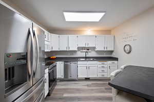 Kitchen with stainless steel appliances, dark countertops, and white cabinetry