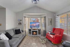 Living room with wood finished floors, vaulted ceiling, and a warm lit fireplace
