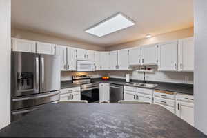 Kitchen with dark countertops, stainless steel appliances, and white cabinetry
