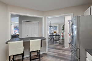 Kitchen with freestanding refrigerator, a breakfast bar, dark wood-type flooring, dark countertops, and white cabinetry