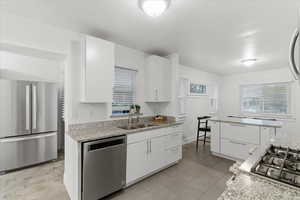Kitchen featuring light stone countertops, stainless steel appliances, white cabinets, and plenty of natural light
