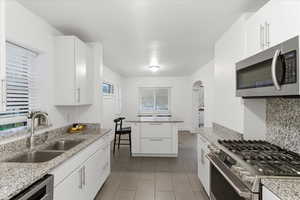 Kitchen featuring appliances with stainless steel finishes, white cabinetry, light stone countertops, arched walkways, and dark tile patterned flooring