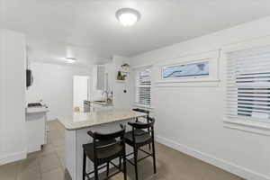 Kitchen with white cabinetry, light stone countertops, a kitchen bar, dark tile patterned floors, and a peninsula
