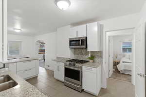 Kitchen with arched walkways, appliances with stainless steel finishes, white cabinets, and light tile patterned floors