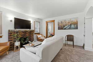 Carpeted living area featuring arched walkways and a brick fireplace