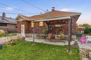 Rear view of property with brick siding, a patio, a chimney, and roof with shingles