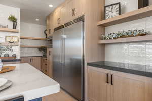 Kitchen featuring open shelves, tasteful backsplash, built in appliances, light brown cabinetry, and dark stone countertops