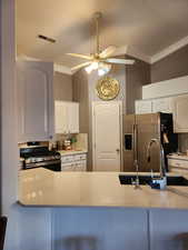 Kitchen featuring ornamental molding, white cabinets, appliances with stainless steel finishes, light stone countertops, and a ceiling fan
