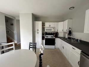 Kitchen featuring dark countertops, electric range oven, tasteful backsplash, white cabinets, and stainless steel dishwasher