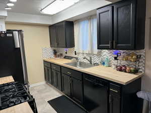 Kitchen with dark cabinets, wood counters, black appliances, and tasteful backsplash