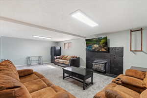 Living area featuring light colored carpet, a textured ceiling, a wood stove, and beam ceiling