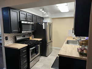Kitchen featuring dark cabinetry, butcher block counters, appliances with stainless steel finishes, and tasteful backsplash