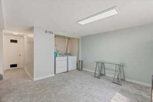 Below grade area featuring light carpet, washer and clothes dryer, and a textured ceiling