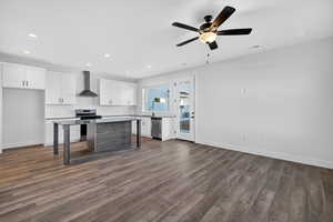 Kitchen featuring white cabinets, backsplash, appliances with stainless steel finishes, wall chimney exhaust hood, and dark wood finished floors