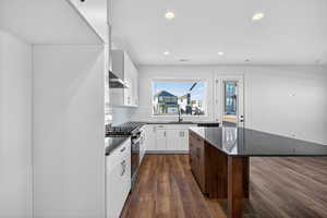 Kitchen featuring dark wood-type flooring, backsplash, white cabinets, stainless steel gas range, and recessed lighting