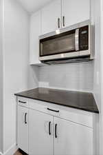 Kitchen featuring white cabinetry, stainless steel microwave, tasteful backsplash, and dark stone countertops