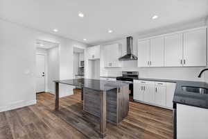 Kitchen with white cabinets, tasteful backsplash, wall chimney range hood, gas range, and a kitchen island