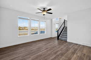 Unfurnished living room with stairs, dark wood-style floors, and a ceiling fan