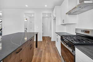 Kitchen with stainless steel range with gas cooktop, extractor fan, light wood-type flooring, white cabinetry, and dark stone countertops