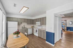 Kitchen featuring white appliances, light countertops, light wood-style flooring, decorative backsplash, and gray cabinets