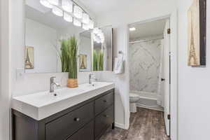 Bathroom with double vanity, shower / tub combo, and dark wood-style floors