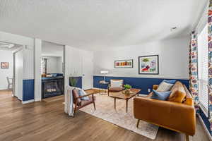 Living area with wood finished floors, a textured ceiling, and a brick fireplace