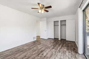 Unfurnished bedroom with two closets, dark wood-style floors, ceiling fan, and a textured ceiling