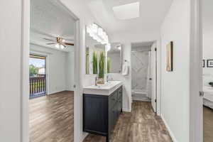 Bathroom with vanity, dark wood-style floors, a textured ceiling, a marble finish shower, and a ceiling fan