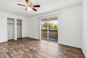 Unfurnished bedroom with multiple closets, dark wood-type flooring, access to exterior, ceiling fan, and a textured ceiling