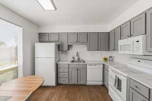 Kitchen featuring gray cabinetry, white appliances, light wood-type flooring, and decorative backsplash