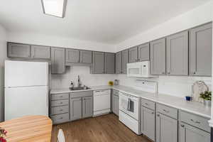Kitchen with gray cabinets, white appliances, and dark wood-type flooring