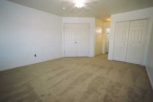 Unfurnished bedroom with carpet flooring, multiple closets, ceiling fan, and attic access