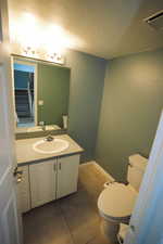 Half bath with a textured ceiling, vanity, and light tile patterned floors