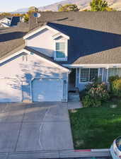 View of front of house featuring roof with shingles, a mountain view, concrete driveway, and a front lawn