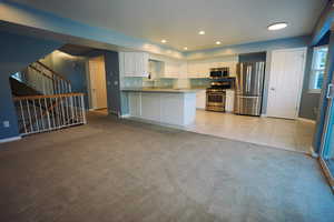 Kitchen featuring white cabinets, stainless steel appliances, light tile patterned floors, light colored carpet, and a peninsula