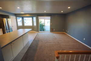 Unfurnished living room featuring a textured ceiling, recessed lighting, light tile patterned floors, and light colored carpet