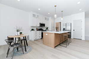 Kitchen featuring a kitchen breakfast bar, white cabinets, stainless steel appliances, a center island with sink, and hanging light fixtures