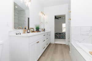 Bathroom featuring double vanity, light wood finished floors, a bath, and a ceiling fan